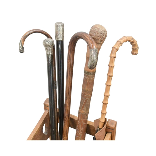 23 - A collection of walking sticks and canes in an Art Nouveau oak stand. Including two silver topped eb... 