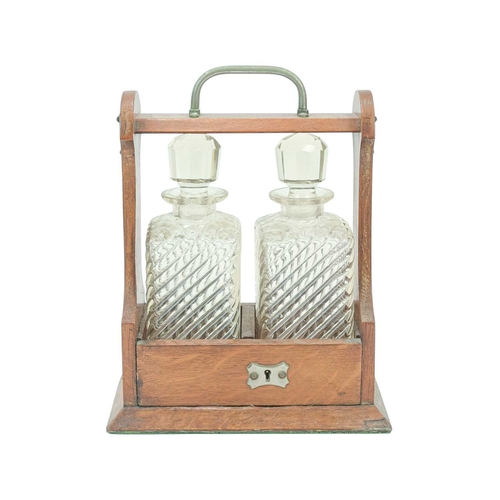 9 - An Edwardian oak two bottle tantalus. With plated mounts, the blown glass decanters with cut stopper... 