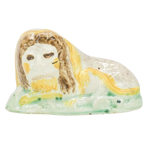 600 - A Pratt ware figure of a recumbent lion. Circa 1820, with ochre, brown, and green painted decoration... 