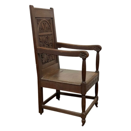 720 - A carved oak wainscot armchair. The panel back dated 1904, and initialled M with a leaf and flowerhe... 