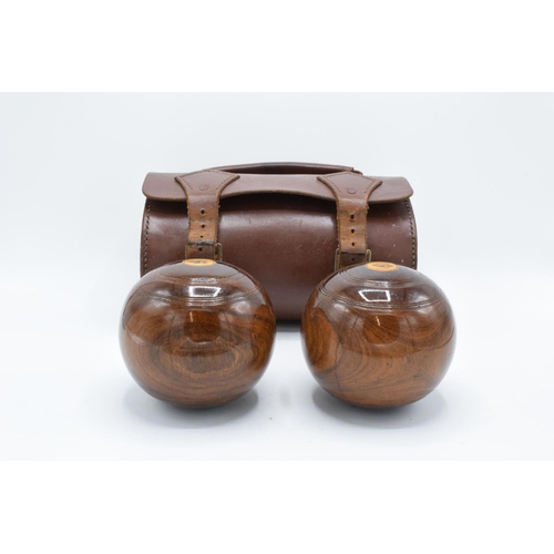 101 - A cased pair of turned 20th century lawn bowls in a leather carry case with monograms.