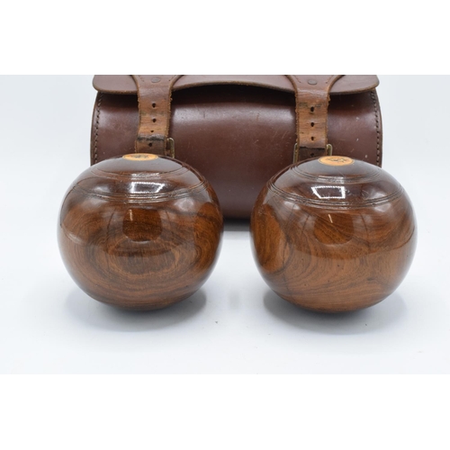 101 - A cased pair of turned 20th century lawn bowls in a leather carry case with monograms.