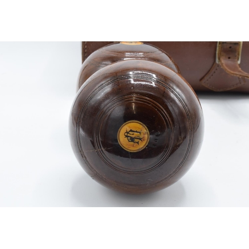 101 - A cased pair of turned 20th century lawn bowls in a leather carry case with monograms.