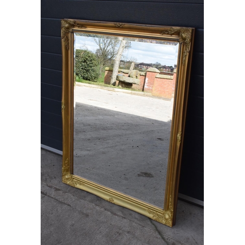 308 - Large 20th century gilt effect wall mirror in ornate wooden frame. 115cm by 91cm. In good condition.