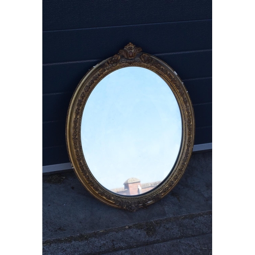 323 - A late 19th/ early 20th century gilt effect wall mirror. 64 cm tall. Oval shape with ornate design. ... 