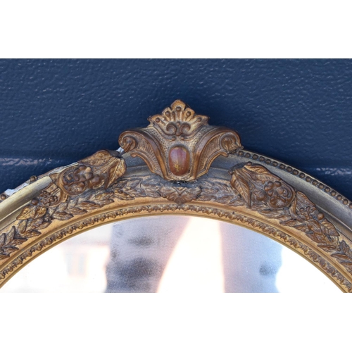 323 - A late 19th/ early 20th century gilt effect wall mirror. 64 cm tall. Oval shape with ornate design. ... 