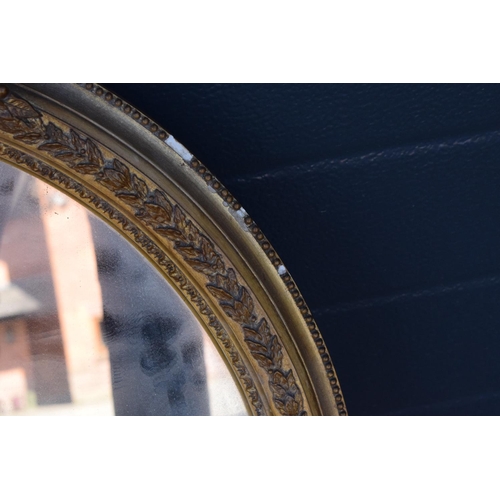 323 - A late 19th/ early 20th century gilt effect wall mirror. 64 cm tall. Oval shape with ornate design. ... 