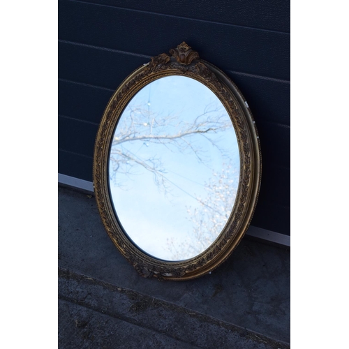 308 - A late 19th/ early 20th century gilt effect wall mirror. 64 cm tall. Oval shape with ornate design. ... 