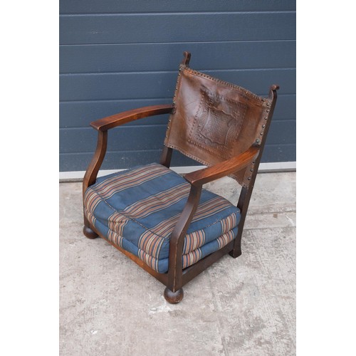 327 - An early 20th century low-seated wooden fireside chair with leather back rest with Coat of Arms or s... 