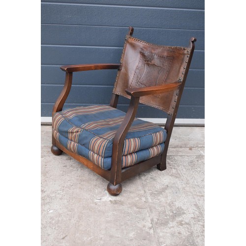 327 - An early 20th century low-seated wooden fireside chair with leather back rest with Coat of Arms or s... 