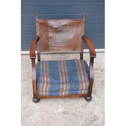 327 - An early 20th century low-seated wooden fireside chair with leather back rest with Coat of Arms or s... 