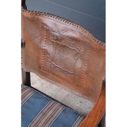 327 - An early 20th century low-seated wooden fireside chair with leather back rest with Coat of Arms or s... 