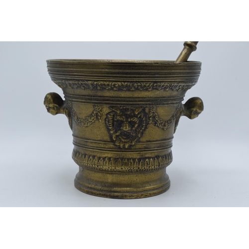 421 - A large antique cast brass mortar and pestle with ornate decoration featuring the devils face. 21cm ... 