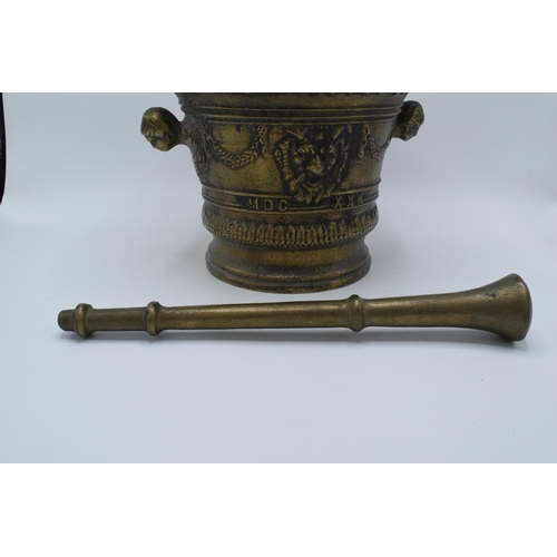 421 - A large antique cast brass mortar and pestle with ornate decoration featuring the devils face. 21cm ... 