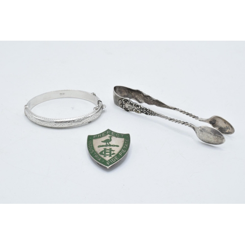 363 - A trio of silver items to include Harrogate College prefect badge, sugar tongs and a child's bangle ... 