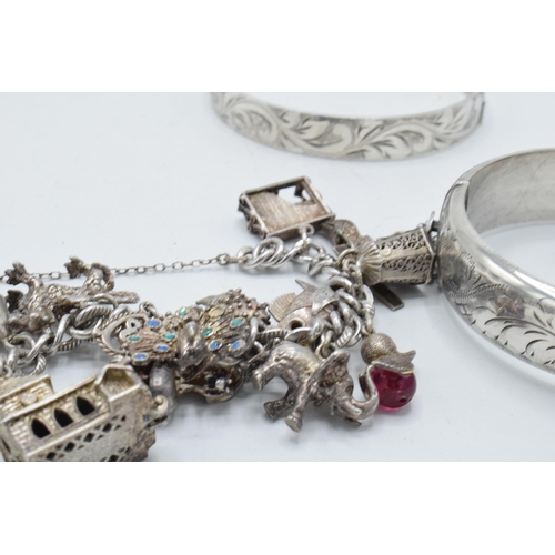 440 - A pair of hallmarked silver bangles, 48.0 grams, together with a white metal charm bracelet with cha... 