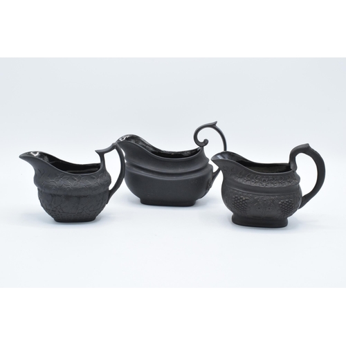 83 - A trio of early to mid 19th century black basalt cream jugs to include 2 examples with detailed flor... 