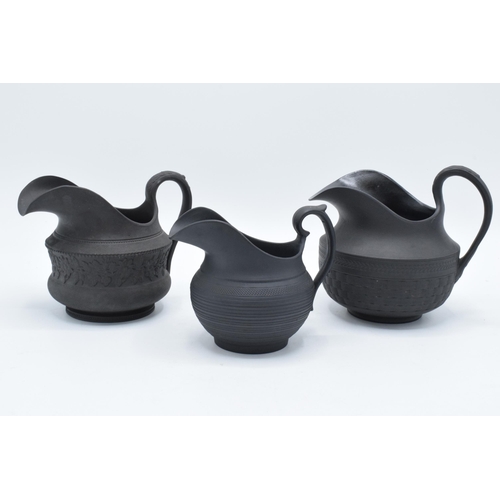 86 - A trio of 19th century black basalt cream jugs to of similar raised forms, one with lace ware design... 