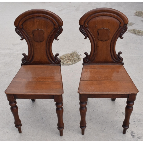 375 - A pair of Victorian oak carved shaped back hall chairs with raised shell motif (2), 86cm tall.