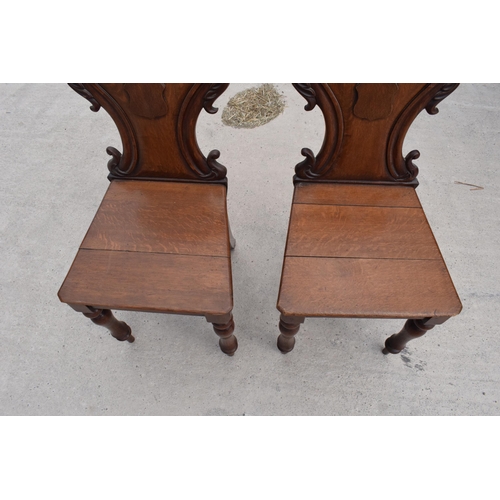 375 - A pair of Victorian oak carved shaped back hall chairs with raised shell motif (2), 86cm tall.