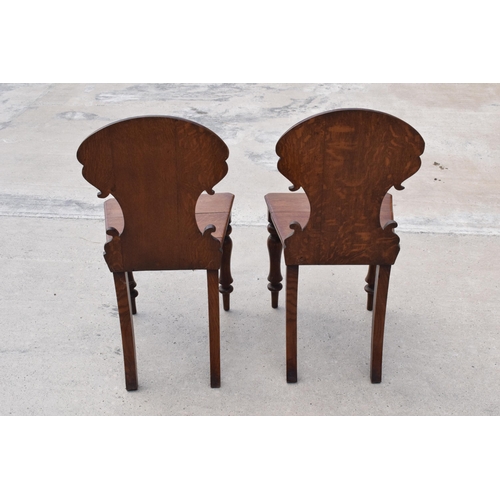 375 - A pair of Victorian oak carved shaped back hall chairs with raised shell motif (2), 86cm tall.