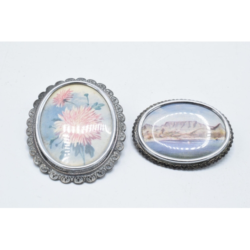 180K - A pair of brooches with a coastal and a floral scene, marked 'TLM' to rear (2).