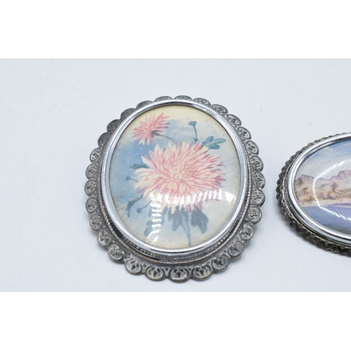 180K - A pair of brooches with a coastal and a floral scene, marked 'TLM' to rear (2).