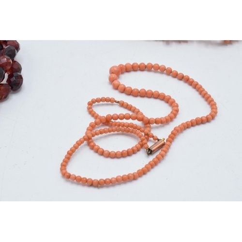 180O - A pair of coral bead necklaces, both with 9ct gold clasps, together with a string of faceted bakelit... 