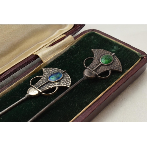 Cased pair of Art Nouveau hat pins with enamelled decoration and hammered Liberty style elements, longest 18cm, boxed.