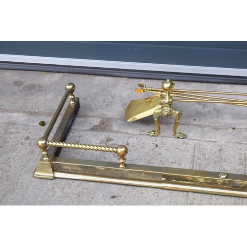 498 - A pair of antique brass fireside dogs along with a companion set and a brass and metal fender.