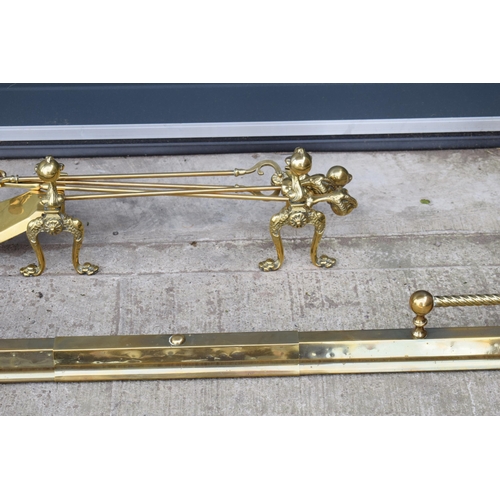 498 - A pair of antique brass fireside dogs along with a companion set and a brass and metal fender.