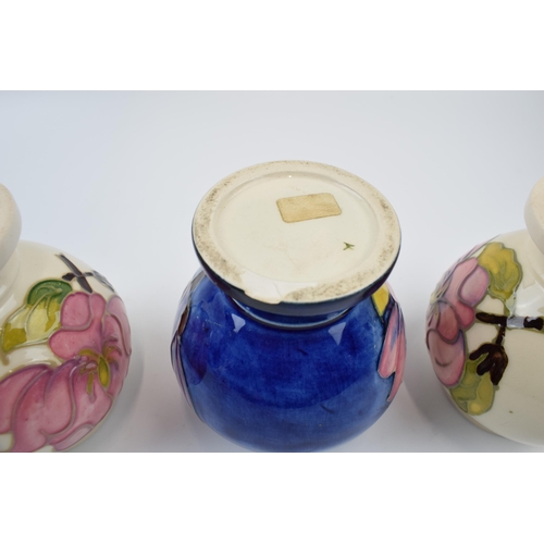 87 - A trio of Moorcroft vases. Two with cream ground with floral design and one in blue. Height 9.5cm.