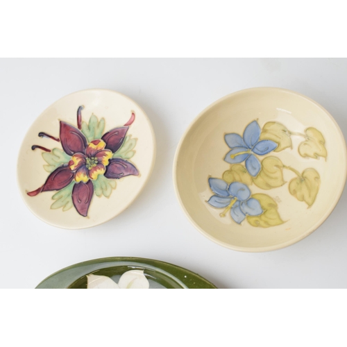 133 - A trio of Moorcroft floral items to include a pin dish, a blue floral bowl and a lily on green ashtr... 