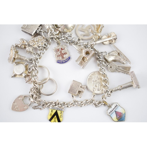 214 - Silver charm bracelet with various charms to include an ice skating boot, rings, a lighthouse and ot... 