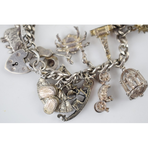 218 - Silver charm bracelet with various charms to include a tankard, a fan, a crab, a bull and others, 69... 