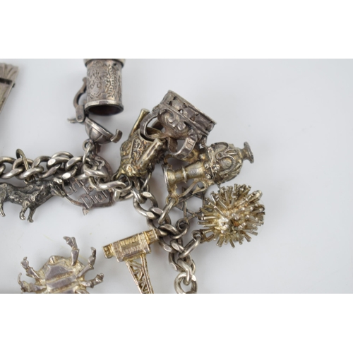 218 - Silver charm bracelet with various charms to include a tankard, a fan, a crab, a bull and others, 69... 