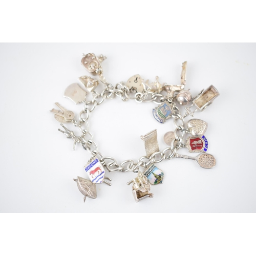 220 - Silver charm bracelet with various charms to include a tennis racket, a film camera, a train, a lady... 