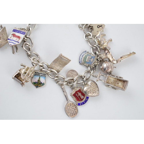 220 - Silver charm bracelet with various charms to include a tennis racket, a film camera, a train, a lady... 