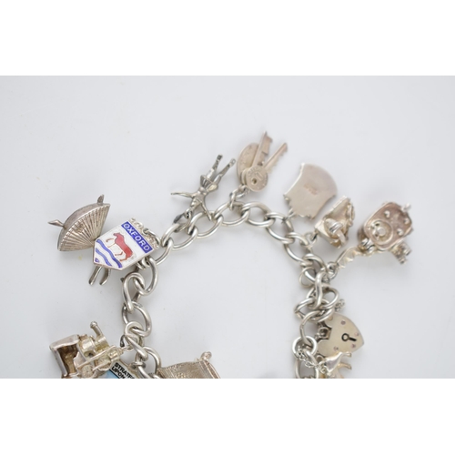 220 - Silver charm bracelet with various charms to include a tennis racket, a film camera, a train, a lady... 