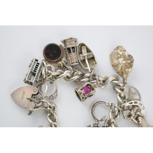 221 - Silver charm bracelet with various charms to include an aeroplane, a tram, a robot, a miner's lamp a... 