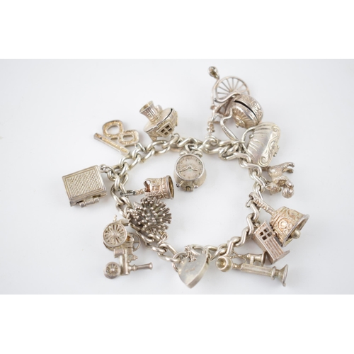 223 - Silver charm bracelet with various charms to include a a bible, a purse, a bell, a telephone and oth... 