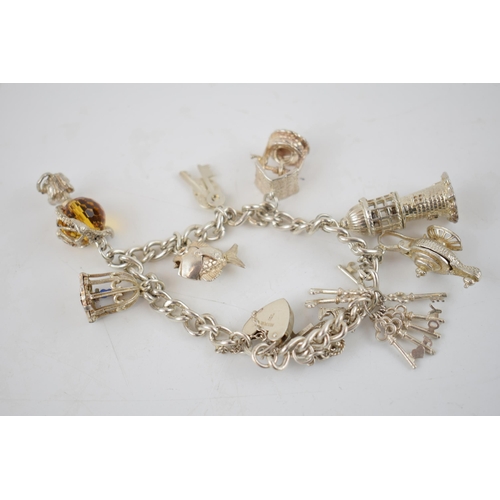 331 - Silver charm bracelet with charms to include a wishing well, a lighthouse, a globe, a bird cage and ... 