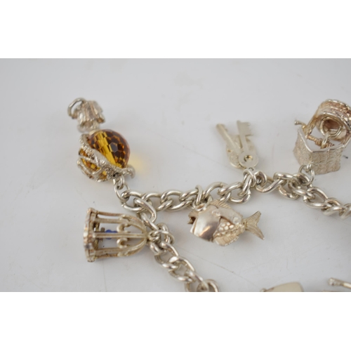 331 - Silver charm bracelet with charms to include a wishing well, a lighthouse, a globe, a bird cage and ... 