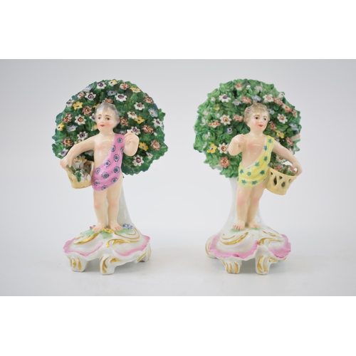 132B - A pair of continental porcelain figures with cherubs amongst foliage holding flowers (2), 13cm tall.