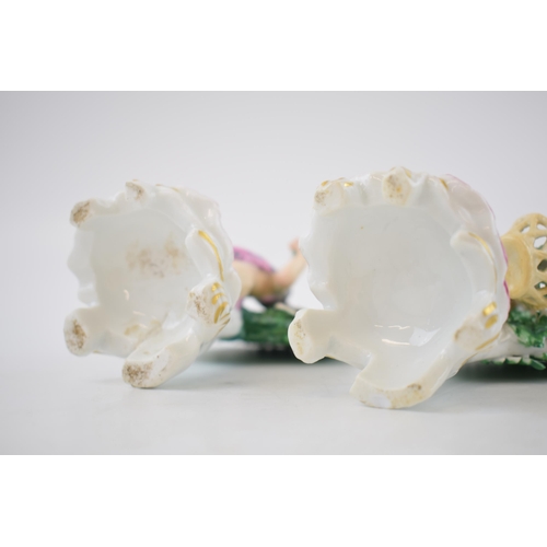 132B - A pair of continental porcelain figures with cherubs amongst foliage holding flowers (2), 13cm tall.