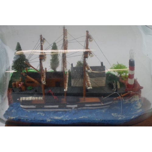 269 - A vintage ship in bottle with scene of lighthouse and houses on wooden plinth.