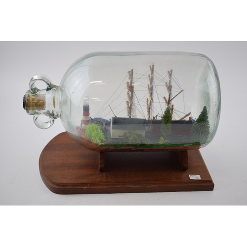 269 - A vintage ship in bottle with scene of lighthouse and houses on wooden plinth.