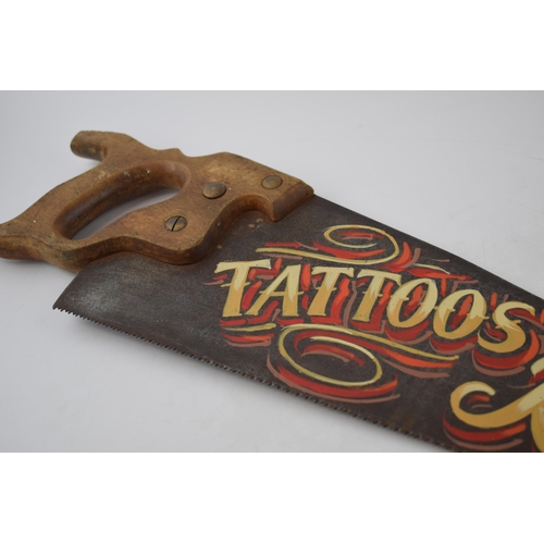 294 - Vintage wooden and metal hand saw with painted 'Tattoos Removed' advertising decor, 66cm wide.