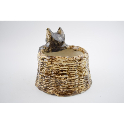 132 - Winstanley pottery cat peaking out of a basket, 18.5cm wide.