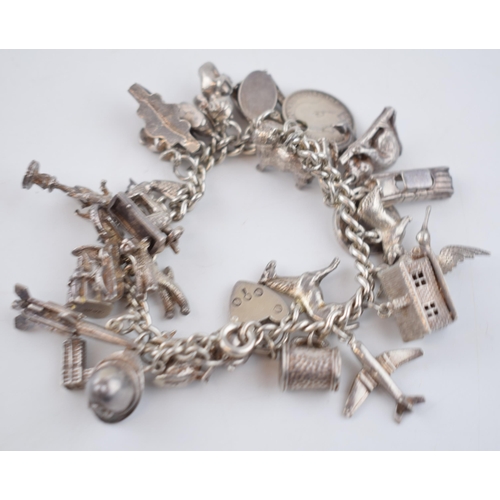 496 - Silver charm bracelet with a collection of charms to include London Bridge, a Bobby's helmet, a plan... 